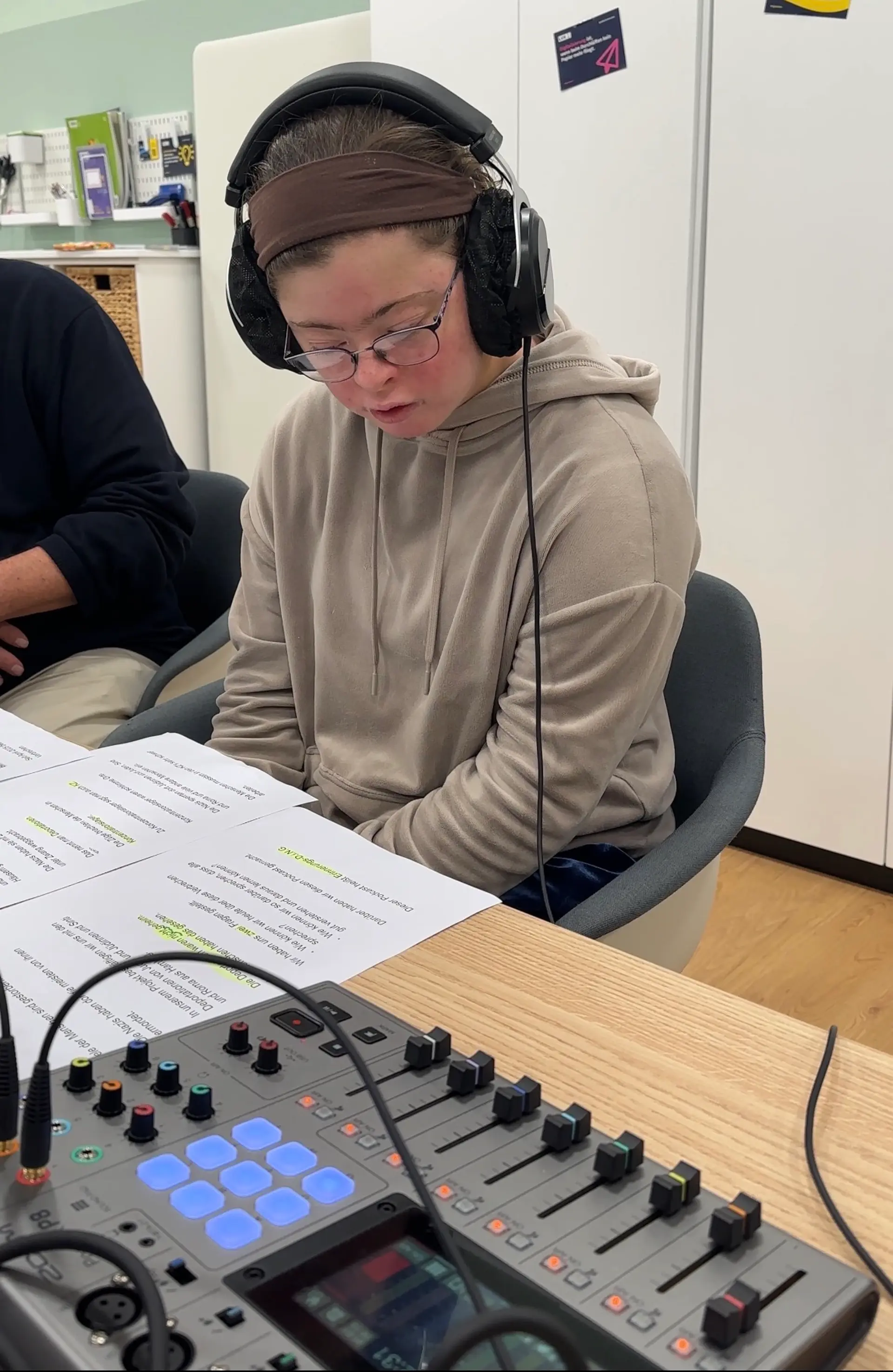 Eine Frau mit Down-Syndrom trägt Overear-Kopfhörer und spricht einen Podcast-Text ein.