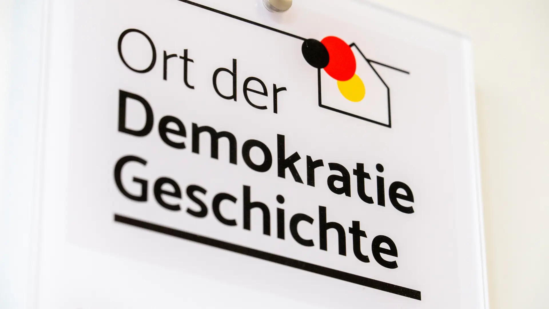 Eine weiße Plakette, auf der steht "Ort der Demokratie Geschichte"