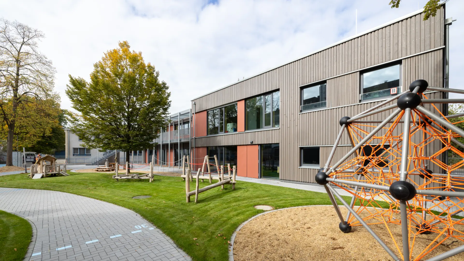 Außenansicht einer LVR-Kita mit Holzfassade und Spielgeräten im Vordergrund.