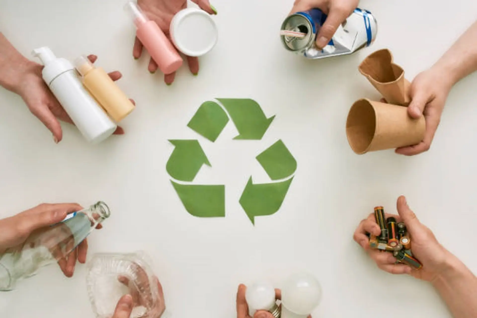 Hände halten verschiedene Abfälle im Keis um ein Recyclingsymbol.