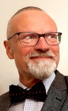 Porträtfotos eines Mannes mit Bart, der freundlich in Richtung des oberen rechten Bildrandes blickt.