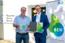 Zweiu Menschen halten eine Urkunde und einen Glaswürfel in der Hand.