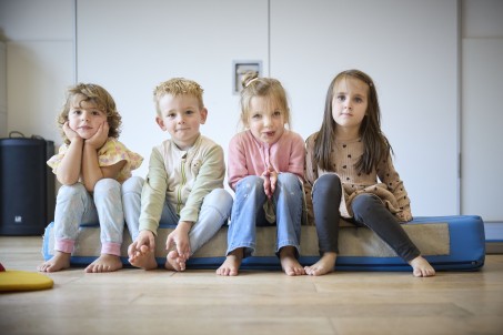 Ein Junge und drei M&auml;dchen im Kindergartenalter sitzen auf einer Turnmatte