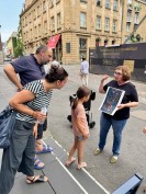 Vor dem Bauzaun der MiQua-Baustelle betrachten ein Mädchen und seine Eltern einen historischen Stadtplan, während die Stadtführerin den Plan erläutert.