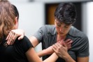Zwei Menschen stehen sich gegenüber. Eine Person drückt zwei Hände an ihr Herz, während sie wiederum ihre andere Hand auf die Schulter ihres Gegenübers legt.