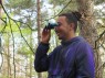 Ein junger Mann steht mit einem Fernglas im Wald