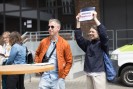 Ein Mann mit orangefarbener und Sonnenbrille steht neben einer jungen Frau, die ein Schild hochhält.
