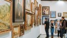 Eine Gruppe Menschen sehen sich in einer Ausstellung verschiedene Gemälde an. 
