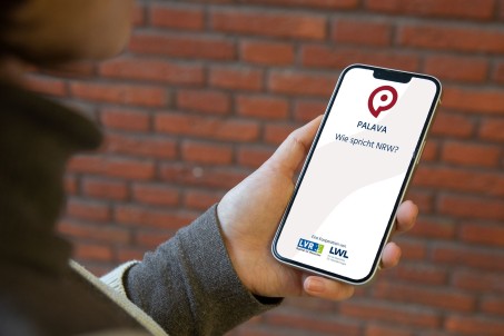 Eine Hand hält ein Mobiltelefon mit der geöffneten PALAVA-App