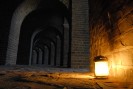 Eine Laterne beleuchtet mit einem warmen Licht einen dunklen Bogengang.