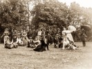 Ein schwarz-weiß Foto von einer Gruppe Menschen in Kostümen. Einige haben Gegenstände in der Hand wie z.B. einen Regenschirm oder einen Stock.