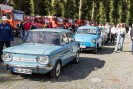 Verschiedene Oldtimer in blauer Farbe in einer Reihe. Ein paar Menschen begutachten sie. Aufgereiht daneben stehen zahlreiche große rote Feuerwehrwagen.