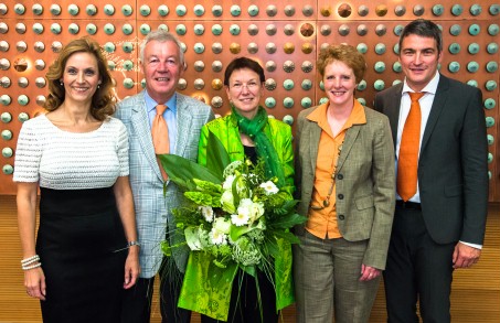 Fünf Personen posieren für die Kamera. Die Frau in der Mitte hält einen Blumenstrauß in der Hand.
