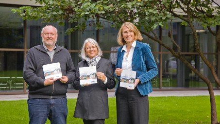 Mann und zwei Frauen halten Broschüre in der Hand