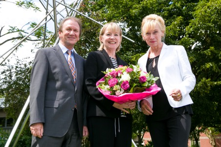 Ein Mann und zwei Frauen vor der Kamera. Die Frau in der Mitte hält einen Blumenstrauß in der Hand.