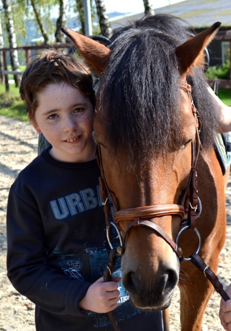 Ein Junge steht neben einem Pferd und lächelt in die Kamera.