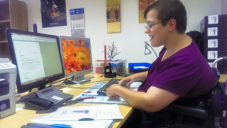 Frau im Rollstuhl im Büro vor PC.