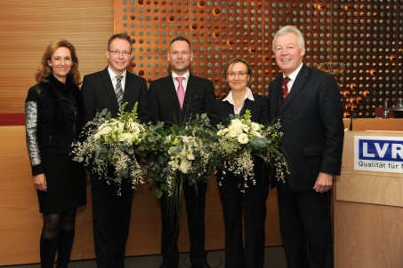 Zwei Frauen und drei Männer stehen in einer Reihe mit Blumensträußen.