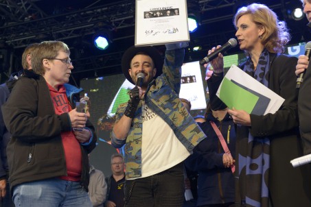 LVR-Direktorin Ulrike Lubek und 2THEUNIVERSE-Sänger Ray Scott Pardue überreichen einen Pokal und eine Urkunde an ein Mitglied der Ottosingers