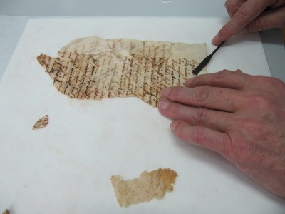 Fragment eines alten Schriftstückes wird mit Spachtel geglättet