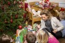 Frau übergibt Kindern Geschenke vor dem Weihnachtsbaum. 