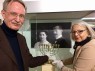 Eine Frau und ein Mann berühren mit weißen Handschuhen einen Leuchter in einer Vitrine.