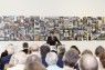 Bild zeigt Publikum vor einem Rednerpult mit einer Frau vor einer großen Fotocollage