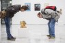 Auf dem Bild sind Besucher der Ausstellung zu sehen. Sie betrachten eine Skulptur aus Holz.