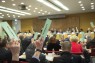 Zwei Personen halten eine Stimmkarte in der Hand. Im Hintergrund Mitglieder der Landschaftsversammlung.