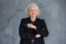 Milena Karabaic im Porträt. Eine Frau mit schulterlangen, grauen Haaren, Brille in der Hand und schwarzem Blazer und Bluse.