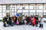 Man sieht eine große Gruppe von Personen im Schnee. Dahinter ist ein Fachwerkhaus zu erkennen. 