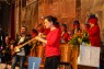 Man sieht eine Frau, die auf einer Bühne Gebärdensprache spricht. Dahinter spielt eine Band Musik. 