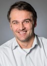 Ein Mann mit kurzem grau-braunem Haar lächelt in die Kamera.