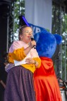 Ninia LaGrande, eine Frau mit Brille und buntem Pullover sowie glitzerndem Rock steht auf einer Bühne und spricht in ein Mikrofon.