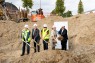 Man sieht fünf Personen auf einer Baustelle mit Schaufeln in den Händen. 