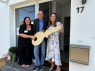 Zwei Frauen und ein Mann halten einen großen Holzschlüssel vor einer Eingangstür
