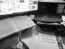 Man sieht einen Schreibtisch, auf dem Blätter mit hebräischer Schrift liegen. Daneben steht ein Computerbildschirm.