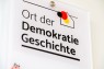 Zu sehen ist die Plakette "Ort der Demokratiegeschichte". Es handelt sich um ein kleines Schild.