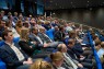 Blick in einen Saal, in dem Menschen sitzen und auf eine Bühne blicken.