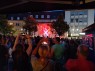 Im Hintergrund ist eine Band auf einer Bühne zu sehen, die rot angeleuchtet wird. Vorne stehen viele Menschen und filmen zum Teil mit ihren Handys. Das Foto wurde abends aufgenommen, es ist bereits relativ dunkel.