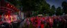 Zu sehen ist der Auftritt einer Band auf einer großen Bühne, die rot beleuchtet ist. Vor der Bühne stehen viele Menschen und feiern mit. Das Bild wurde bei Dunkelheit aufgenommen.