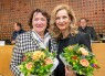 Zwei Frauen stehen mit Blumenstr&auml;u&szlig;en in den H&auml;nden nebeneinander und l&auml;cheln in die Kamera.