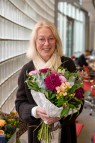 Eine Frau mit blonden mittellangen Haaren mit Blumenstrau&szlig; in der Hand l&auml;chelt in die Kamera.