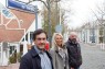Zwei Männer und eine Frau stehen auf einer Straße und lächeln in die Kamera. 