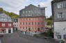 Blick auf das Rote Haus Monschau von der Straße aus in Frontansicht. Zu sehen ist ein fünfstöckiges Haus mit roter Fassade und vielen Fenstern.