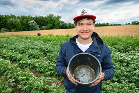 Junger Mann mit einem Eimer auf einem Feld.