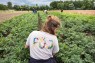 Eine junge Frau sitzt auf einem Feld. T-Shirt-Aufschrift: F&Ouml;J.