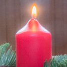 Eine brennende Rote Kerze auf einem Tisch, umgeben von Tannenzweigen, Walnüssen und Äpfeln