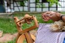 Ein Spinnrad in Betrieb. Es sind nur zwei Hände zu sehen, die gerade einen Faden spinnen. 