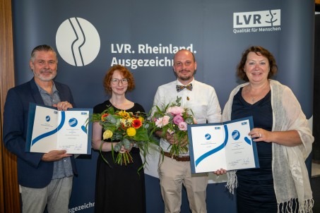 Vier Personen stehen nebeneinander: Links ein Mann, der eine Urkunde h&auml;lt. Neben ihm eine Frau, die einen Blumestrau&szlig; h&auml;lt. Daneben ein Mann mit einem Blumenstrau&szlig; und ganz rechts steht eine Frau mit einer Urkunde in der Hand.